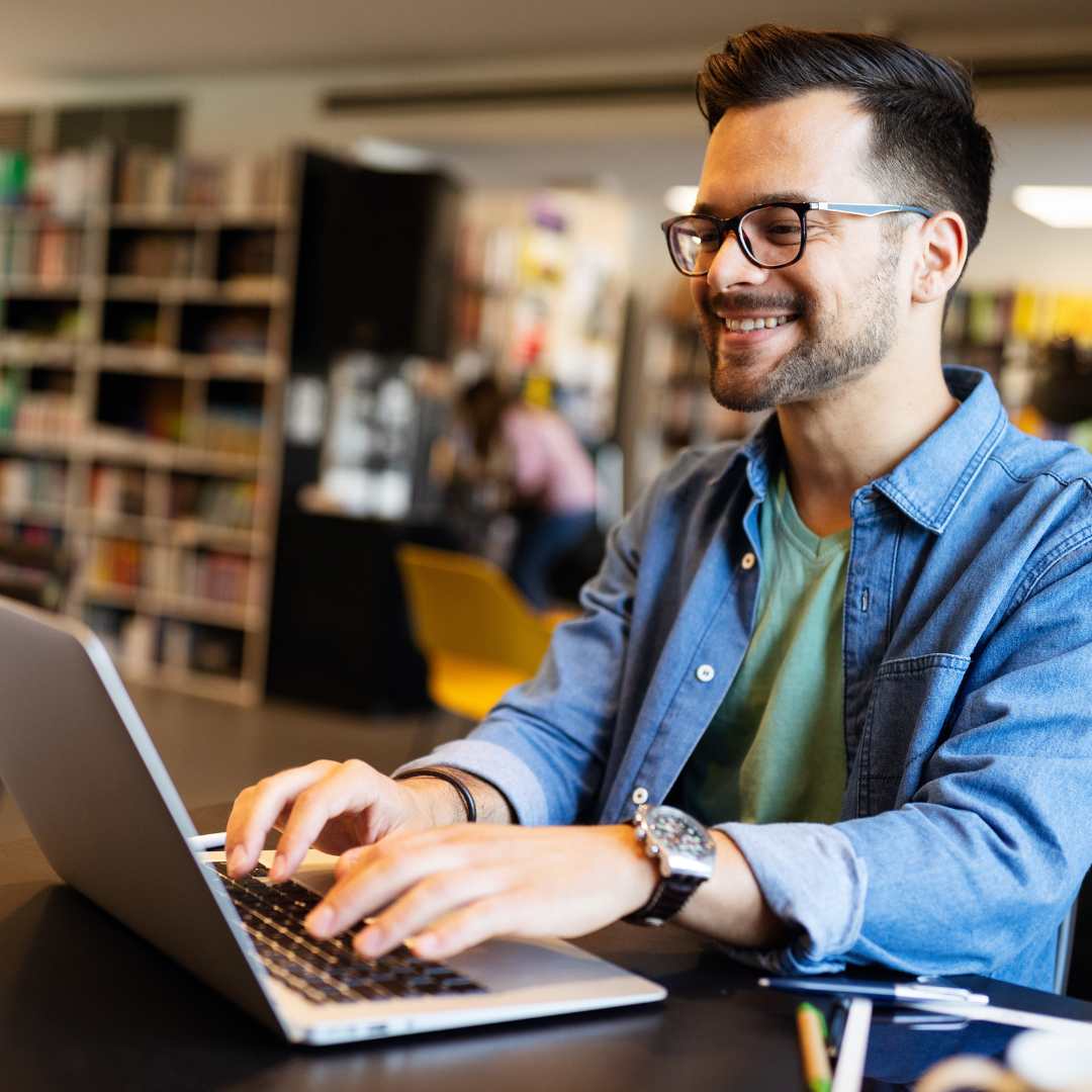 A man sitting behind a laptop, smiling at the screen.